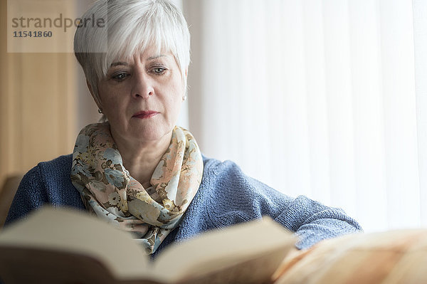 Porträt einer älteren Frau  die auf der Couch sitzt und ein Buch liest.