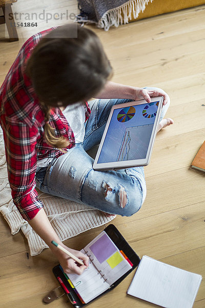 Junge Frau zu Hause  die mit dem digitalen Tablett arbeitet und Notizen macht.