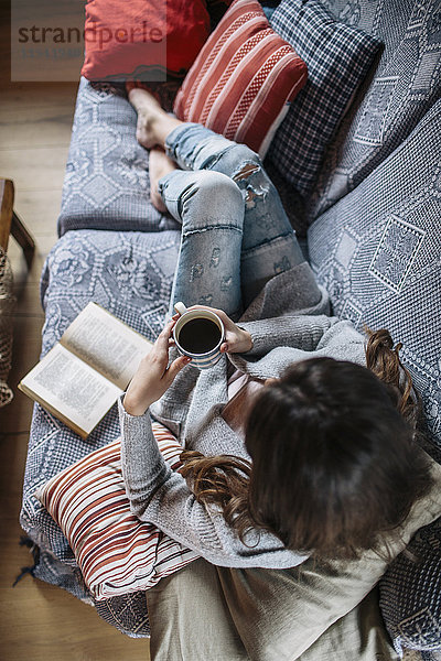 Junge Frau zu Hause bei einer Tasse Kaffee und einem Buch entspannen