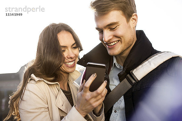 Lächelndes junges Paar schaut auf das Smartphone im Freien