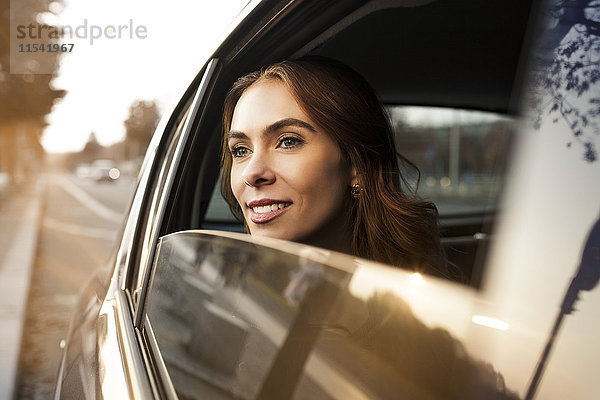 Lächelnde junge Frau schaut aus dem Autofenster