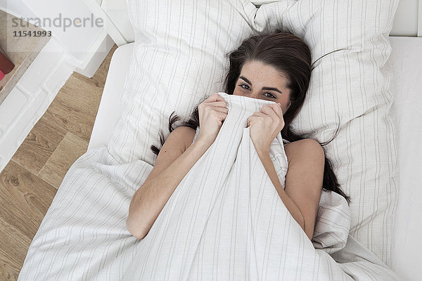 Lächelnde junge Frau im Bett liegend