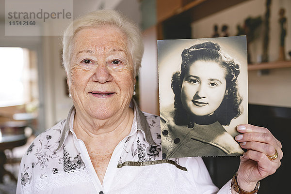 Porträt einer älteren Frau  die ein altes Bild von sich selbst zeigt.