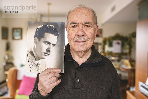 Portrait eines älteren Mannes  der ein altes Bild von sich zeigt.