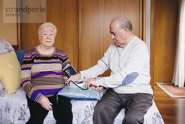 Älterer Mann  der den Blutdruck seiner Frau zu Hause kontrolliert.