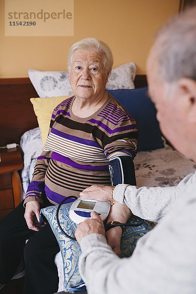 Älterer Mann  der den Blutdruck seiner Frau zu Hause kontrolliert.