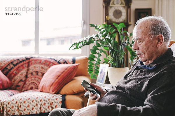 Senior Mann im Wohnzimmer sitzend mit Smartphone