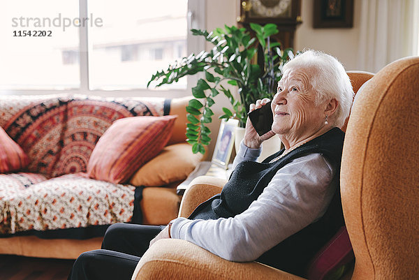 Lächelnde Seniorin beim Telefonieren mit dem Smartphone zu Hause