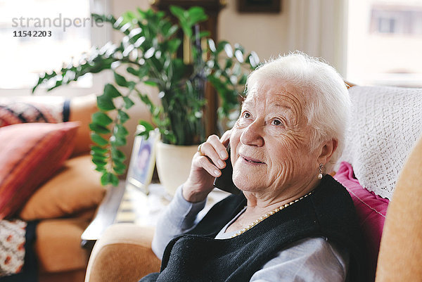 Porträt einer lächelnden Seniorin beim Telefonieren mit dem Smartphone zu Hause