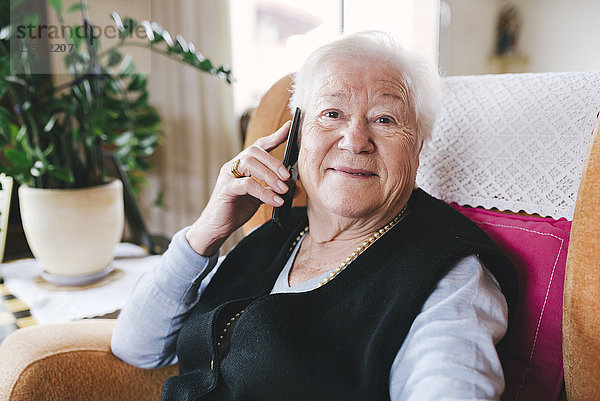 Porträt einer lächelnden Seniorin beim Telefonieren mit dem Smartphone zu Hause