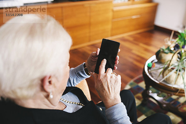 Seniorin sitzend im Wohnzimmer mit Smartphone