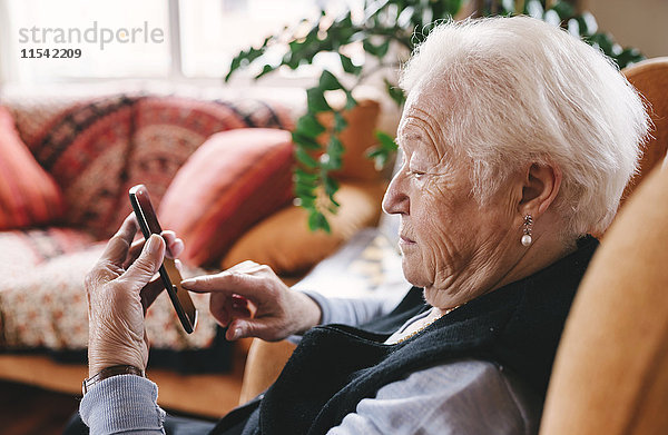 Seniorin sitzend im Wohnzimmer mit Smartphone