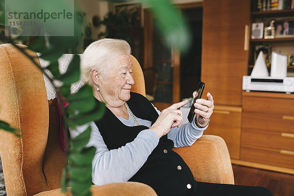 Seniorin sitzend im Wohnzimmer mit Smartphone