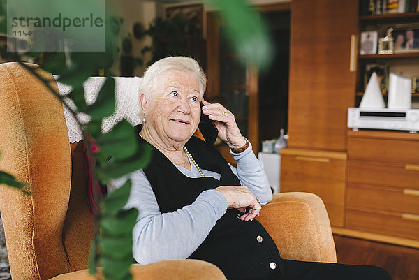 Porträt einer lächelnden Seniorin beim Telefonieren mit dem Smartphone zu Hause