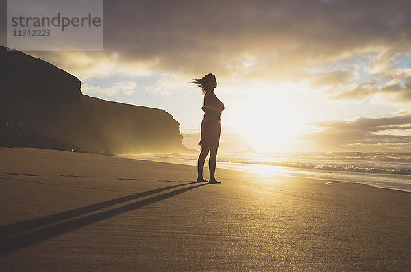 Spanien  Fuerteventura  Frau am Strand stehend bei Sonnenuntergang