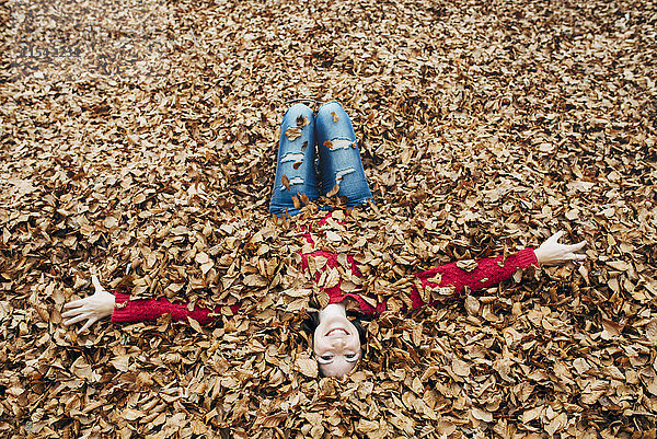 Frau mit ausgestreckten Armen auf Waldboden liegend mit Herbstblättern bedeckt