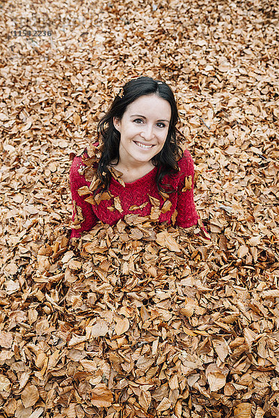Porträt einer lächelnden Frau  die auf einem mit Herbstblättern bedeckten Waldboden sitzt.