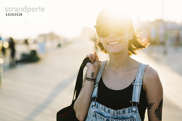 USA  New York  Coney Island  lächelnde junge Frau an der Strandpromenade bei Sonnenuntergang