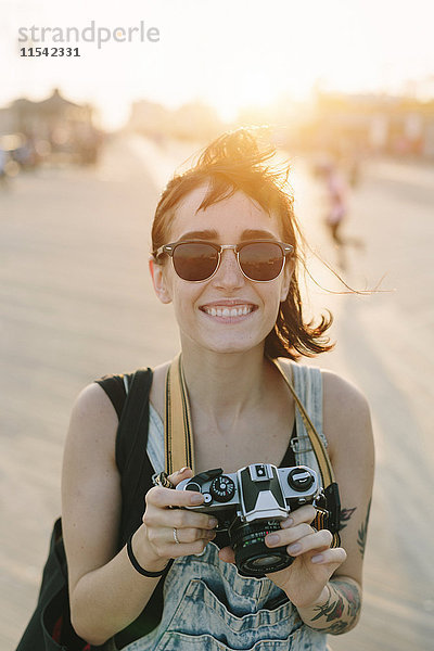 USA  New York  Coney Island  lächelnde junge Frau beim Fotografieren bei Sonnenuntergang