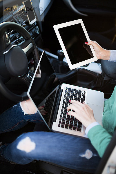 Frau arbeitet im Auto mit digitalem Tablett und Laptop