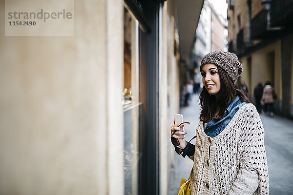 Spanien  Barcelona  lächelnde junge Frau in der Stadt mit Blick auf das Schaufenster