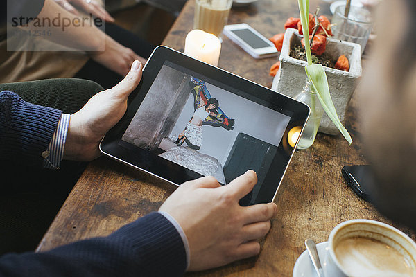 Mann in einem Café mit Bild auf digitalem Tablett für Freunde