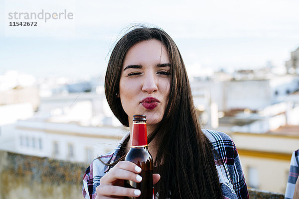 Spanien  Jerez de la Frontera  Porträt einer zwinkernden jungen Frau mit Bierflasche und schmollendem Mund
