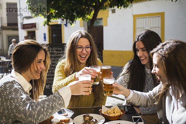 Vier glückliche Freunde stoßen mit Bier in einem Straßencafé an.