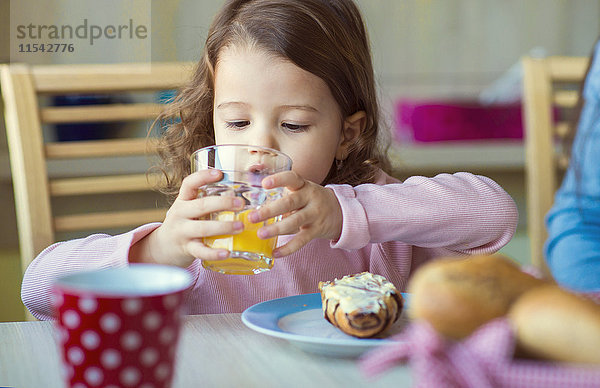 Porträt eines kleinen Mädchens  das am Frühstückstisch ein Glas Orangensaft trinkt.