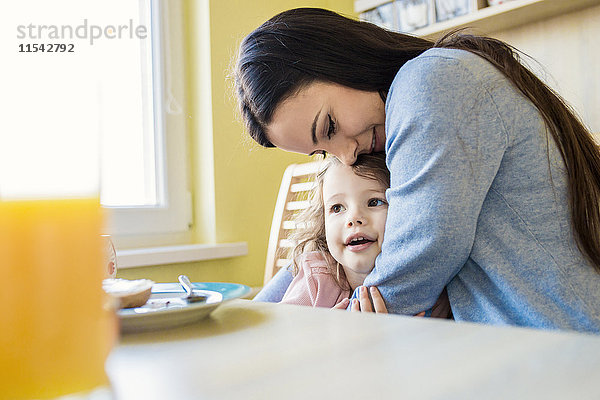 Mutter und ihre kleine Tochter beim Kuscheln am Frühstückstisch