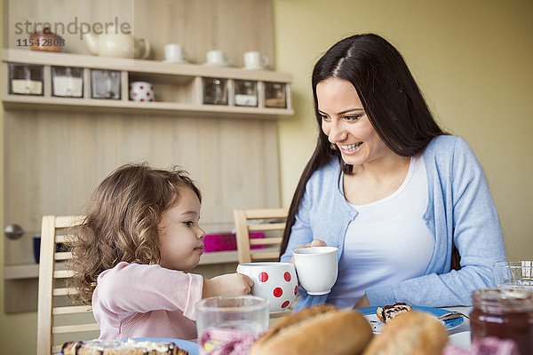 Mutter und ihre kleine Tochter stoßen mit ihren Tassen am Frühstückstisch an.