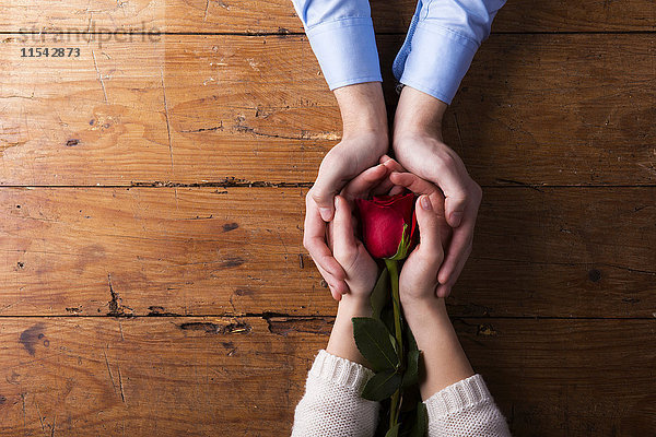 Hände eines jungen Paares mit roter Rose
