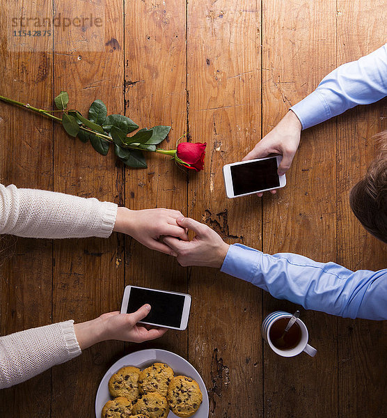 Junges Paar  das Händchen hält und sein Smartphone.