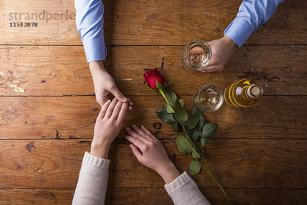 Hände eines jungen Paares mit roter Rose und einer Flasche Weißwein