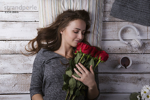 Glückliche junge Frau liegt auf dem Boden und riecht rote Rosen.
