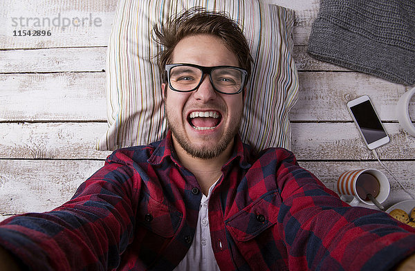 Porträt eines schreienden jungen Mannes  der auf dem Boden liegt und einen Selfie nimmt.