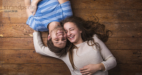 Lachendes junges Paar entspannt sich gemeinsam auf dem Holzboden