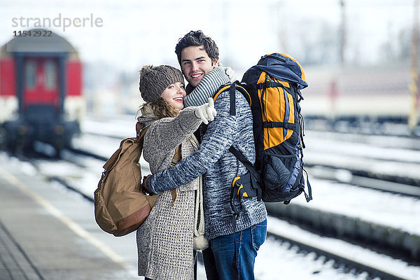Lächelndes junges Paar umarmt auf dem Bahnsteig