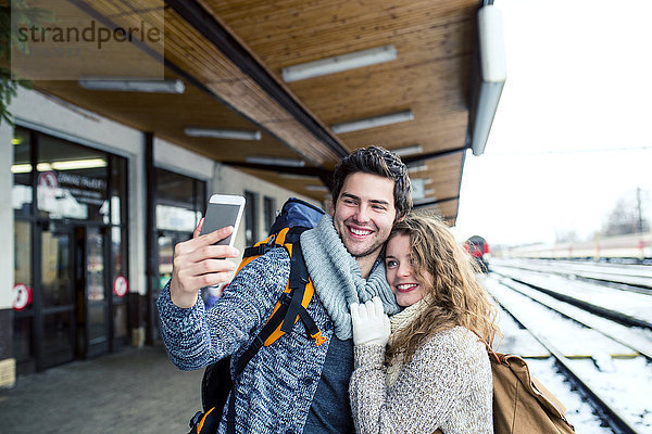 Glückliches junges Paar auf dem Bahnsteig mit einem Selfie