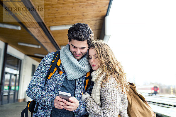 Junges Paar auf dem Bahnsteig mit Blick auf das Handy
