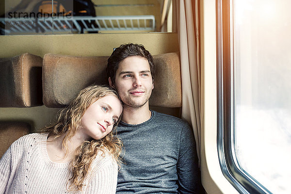 Lächelndes junges Paar im Zugwagen aus dem Fenster schauend