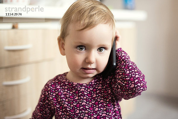 Portrait eines blonden Kleinkindes beim Spielen mit dem Smartphone