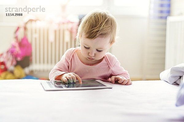 Kleinkind spielt mit digitalem Tablett auf dem Bett