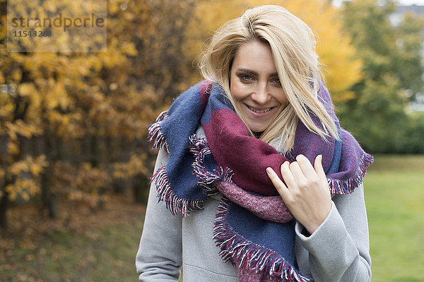Porträt einer fröhlichen jungen Frau mit modischem Schal im herbstlichen Park