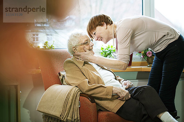 Erwachsene Tochter begrüßt ihre Mutter mit Alzheimer-Krankheit in ihrem Zimmer im Altersheim