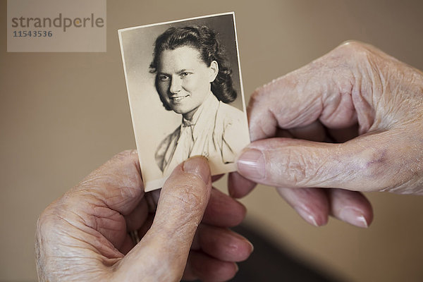 Hände einer älteren Frau  die alte Fotos von sich selbst hält.