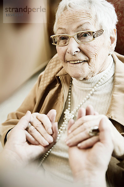 Porträt einer älteren Frau mit Alzheimer-Krankheit  die die Hände ihrer erwachsenen Tochter hält.