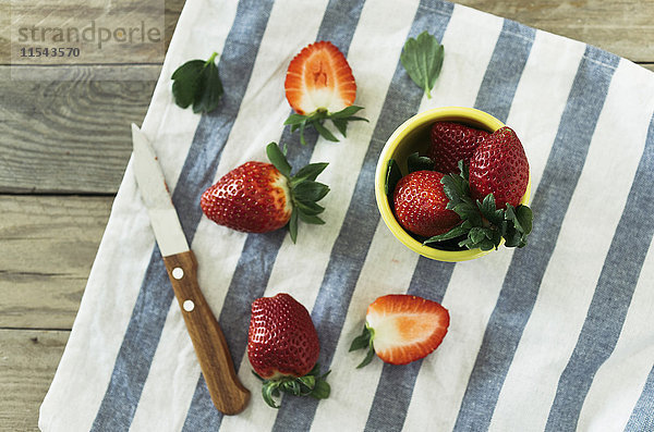 Ganze und geschnittene Erdbeeren und ein Küchenmesser auf gestreiftem Tuch