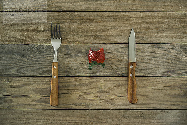 Gabel  Messer und eine gebissene Erdbeere auf Holz