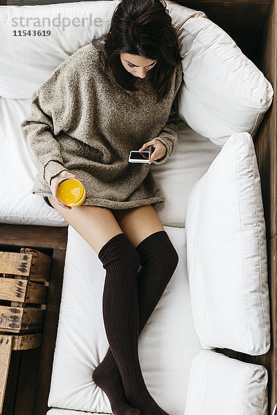 Frau entspannt mit Smartphone und einem Glas Orangensaft